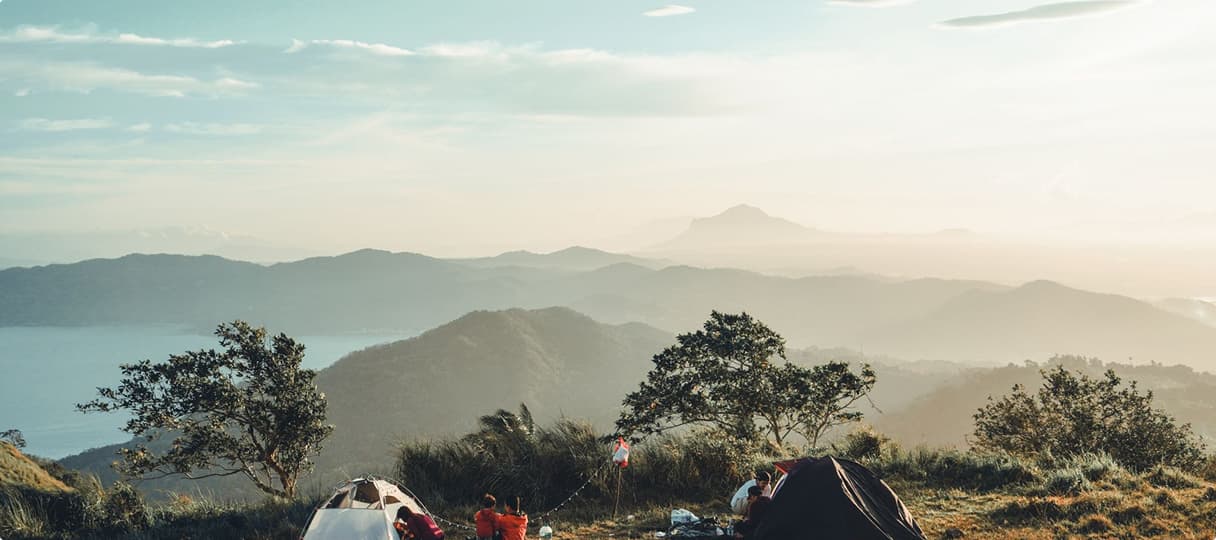 Tents pitched on a grassy ridge above misty Sahyadri hills